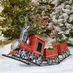 a small red toy train on top of snow covered ground next to a christmas tree