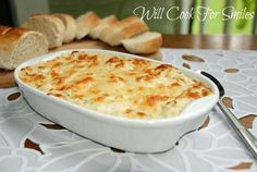 a casserole dish with cheese and bread in the background on a tablecloth