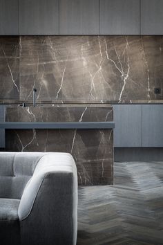 a modern kitchen with marble counter tops and grey cabinets, along with a gray couch in the foreground