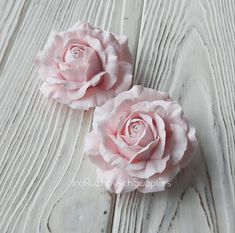 two pink roses sitting on top of a white wooden table next to each other,