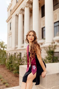 a beautiful young woman sitting on top of a cement wall next to a tall building