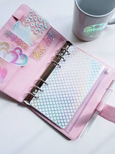 a pink binder with lots of stickers on it next to a coffee cup