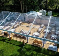 an outdoor dining area with tables and chairs under a clear tent on the grass in front of trees