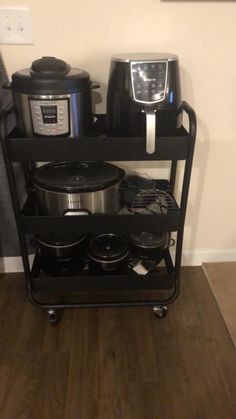 a black cart with pots and pans on it in front of a wall mounted clock