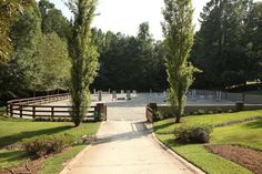 an empty path leading to a horse stable with trees in the foreground and fencing on either side