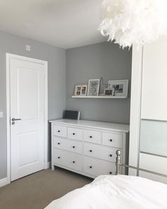 a bedroom with gray walls and white dressers in the corner next to a bed