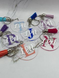 six personalized acrylic key chains with tassels are arranged on a marble surface