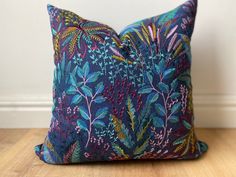 a blue pillow with colorful leaves on it sitting on a wooden floor next to a white wall