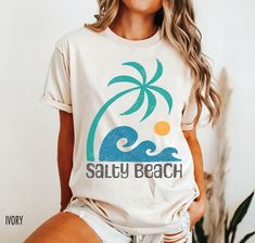 Embrace island vibes with our Salty Beach retro summer shirt featuring a tropical palm tree and wave graphic, reminiscent of vintage surf culture.  The graphic on this shirt is faded and distressed to create a vintage look. We use professional quality DGT printing on all our apparel. Direct-to-garment, or DTG, is a high quality printing method that sprays ink directly onto the garment so there is no peeling or cracking. This fabulous graphic will be printed on a Comfort Colors Unisex T-Shirt. Pl Tropical Palm Tree Print Vacation Top, Tropical Palm Tree Print Tops For Vacation, Summer Tropical Surfing T-shirt, Tropical Print Beach Shirt, Tropical Palm Tree Print Tops For Beach Party, Tropical Print T-shirt For Vacation, Summer Tops With Palm Tree Print For Surfing, Tropical Tops With Palm Tree Print For Beach Party, Beach Party Top With Palm Tree Print