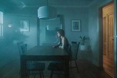 a woman sitting at a table in the middle of a room with blue light coming from behind her