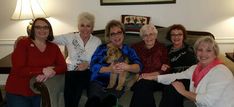 four women sitting on a couch with a dog in their lap and one woman holding her arm around the other