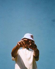 a man wearing a pink hat and holding his hands up to his face while standing in front of a blue sky