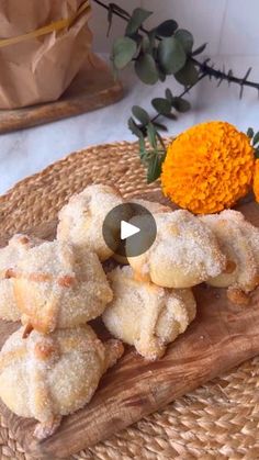 a wooden cutting board topped with powdered sugar pastries next to an orange flower