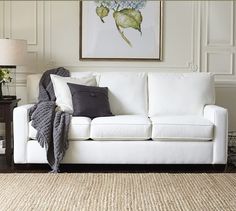 a living room with a white couch and throw pillows on the floor next to a lamp