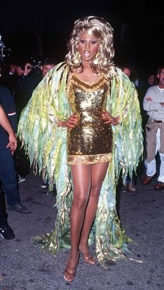 a woman in a gold and green costume walking down the street with people behind her