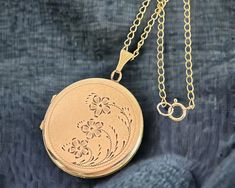 "Description: A wonderful vintage round gold filled locket necklace with an ornately decorated etched front that features three flowers with leaves and curved stems of three different lengths that grow up and curl around the right side of this locket. All round the circular locket front is a fine etched line that frames the floral design. The back of this retro locket is plain with no design and has a shiny finish. The fanned bale is a decorative one with some angled lines.  This larger sized lo Floral Flower Design, Birthstone Necklace Mothers, Flowers With Leaves, Three Flowers, Vintage Lockets, White Photos, Floral Flower, Birthstone Necklace, Locket Necklace