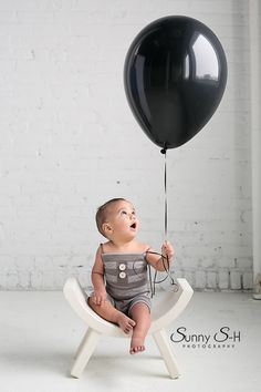 a baby sitting in a chair with a black balloon