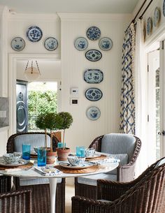 a dining room with wicker chairs and plates hanging on the wall above it's table