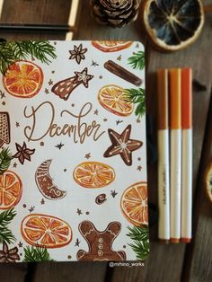 a notebook with oranges and writing on it next to pencils, pine cones and other decorations