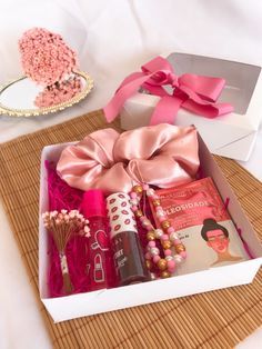 an open box with various items in it on a bamboo mat next to a pink bow