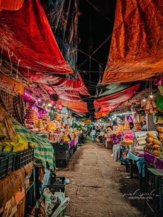 an open air market with lots of fruits and vegetables on the tables under red tarps