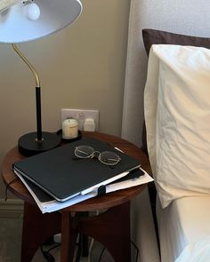 a book, eyeglasses and lamp on a small table in a hotel room