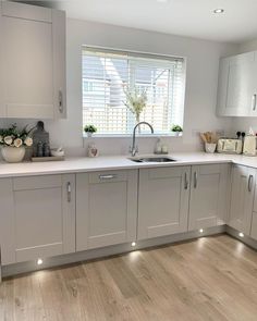 a kitchen with white cabinets and wooden floors is pictured in this image, there are flowers on the window sill