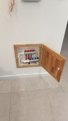 an open wooden cabinet with toothbrushes and other items in it on the wall