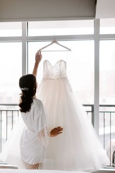 a woman is looking at a wedding dress on a hanger in front of a window