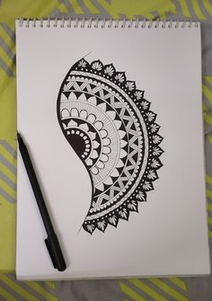 a spiral notebook with a black and white paisley design on the cover next to a pen