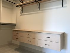 an empty walk - in closet with white walls and wooden drawers, hanging rails on the ceiling