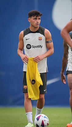 a man standing next to a soccer ball on top of a green field with a yellow towel