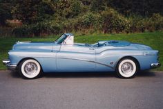 an old blue car parked on the side of the road in front of some bushes