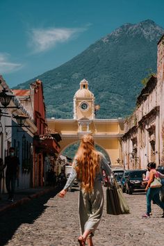 a woman walking down a cobblestone street with a clock tower in the background