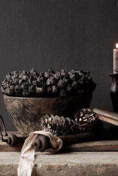 a wooden bowl filled with pine cones next to a candle