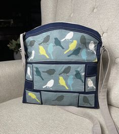 a blue and yellow bird print purse sitting on top of a gray couch next to a white chair