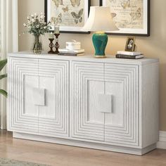 a white sideboard with two pictures on the wall above it and a lamp next to it