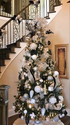 a decorated christmas tree sitting in the middle of a living room next to a stair case