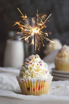 a cupcake with white frosting and sprinkles on top is being lit by a sparkler