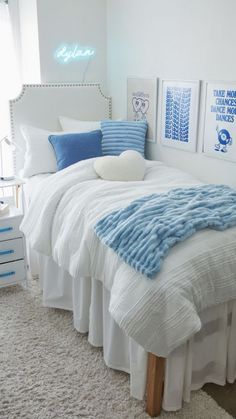 a white bed with blue and white decor in a small room, along with two framed pictures on the wall