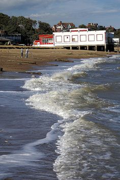 the waves are coming in to the shore and people walking on the beach near the water