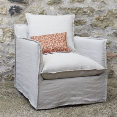 a white chair with a pillow on top of it next to a stone wall and floor