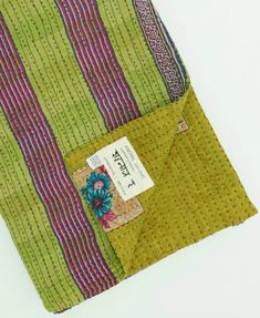 a green and pink striped fabric with a tag on it's pocket, sitting on a white surface