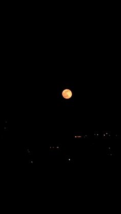 a full moon is seen in the dark sky above some buildings at night with no clouds