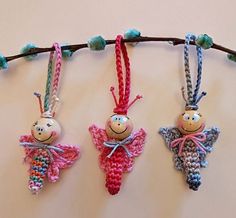 three crocheted dolls are hanging on a twig and one is wearing a pink dress