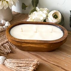 a wooden bowl filled with white candles on top of a table next to flowers and twine