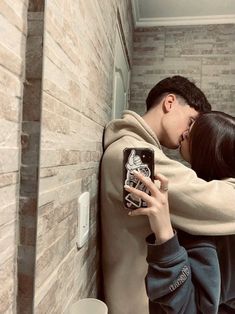 a man and woman kissing while taking a selfie in a bathroom with a brick wall behind them