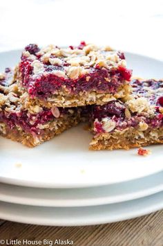 three pieces of berry crumble bars stacked on top of each other in front of the rest of the plate