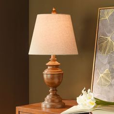 a lamp sitting on top of a wooden table next to a mirror and flowers in a vase