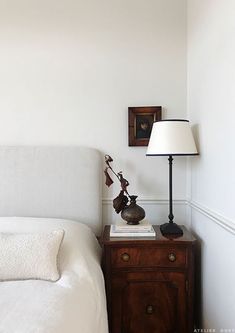 a white bed sitting next to a lamp on top of a wooden night stand in a bedroom